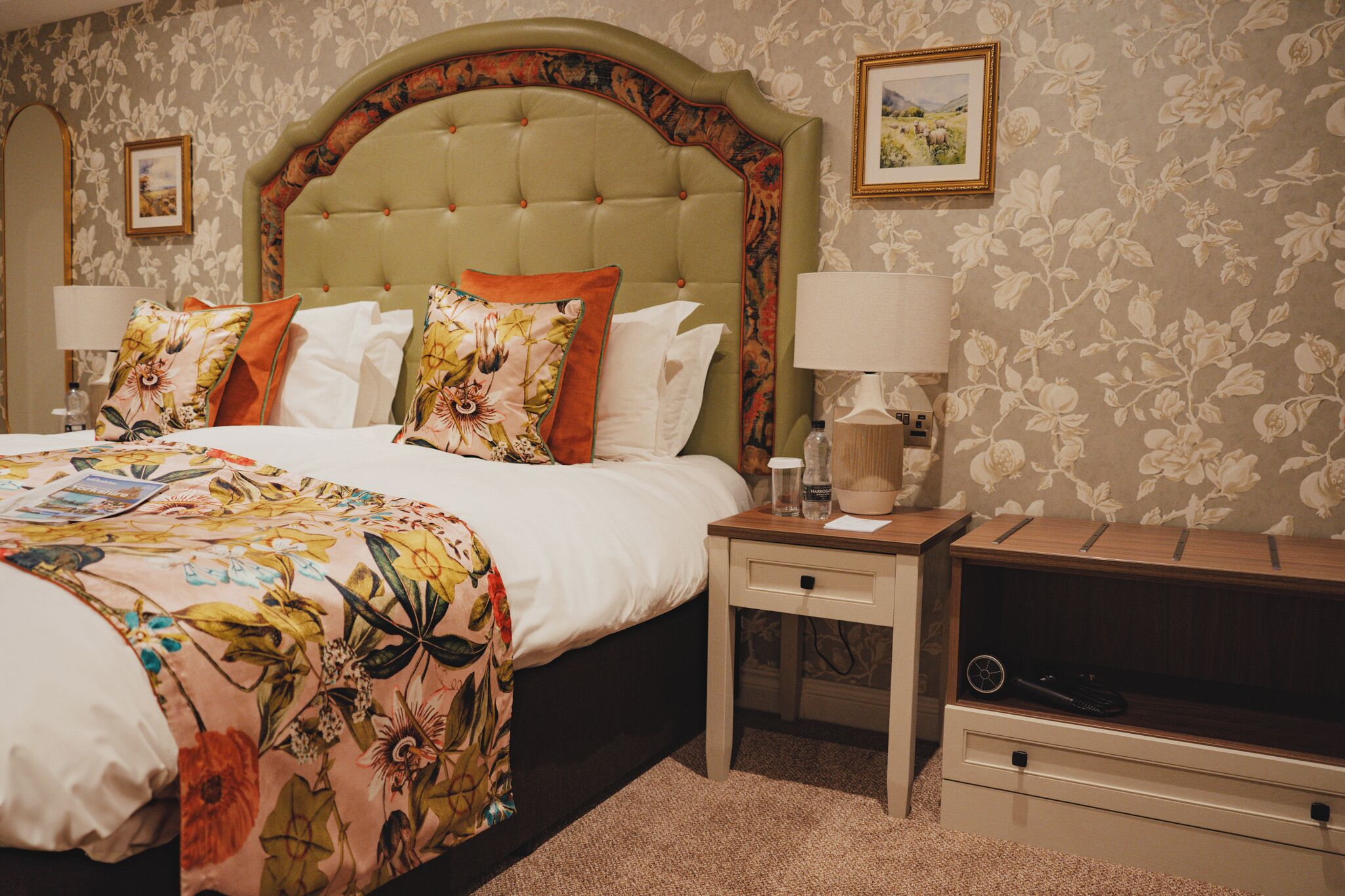A hotel room with a large bed, floral bedspread, two bedside tables with lamps, a wooden nightstand, and a TV.
