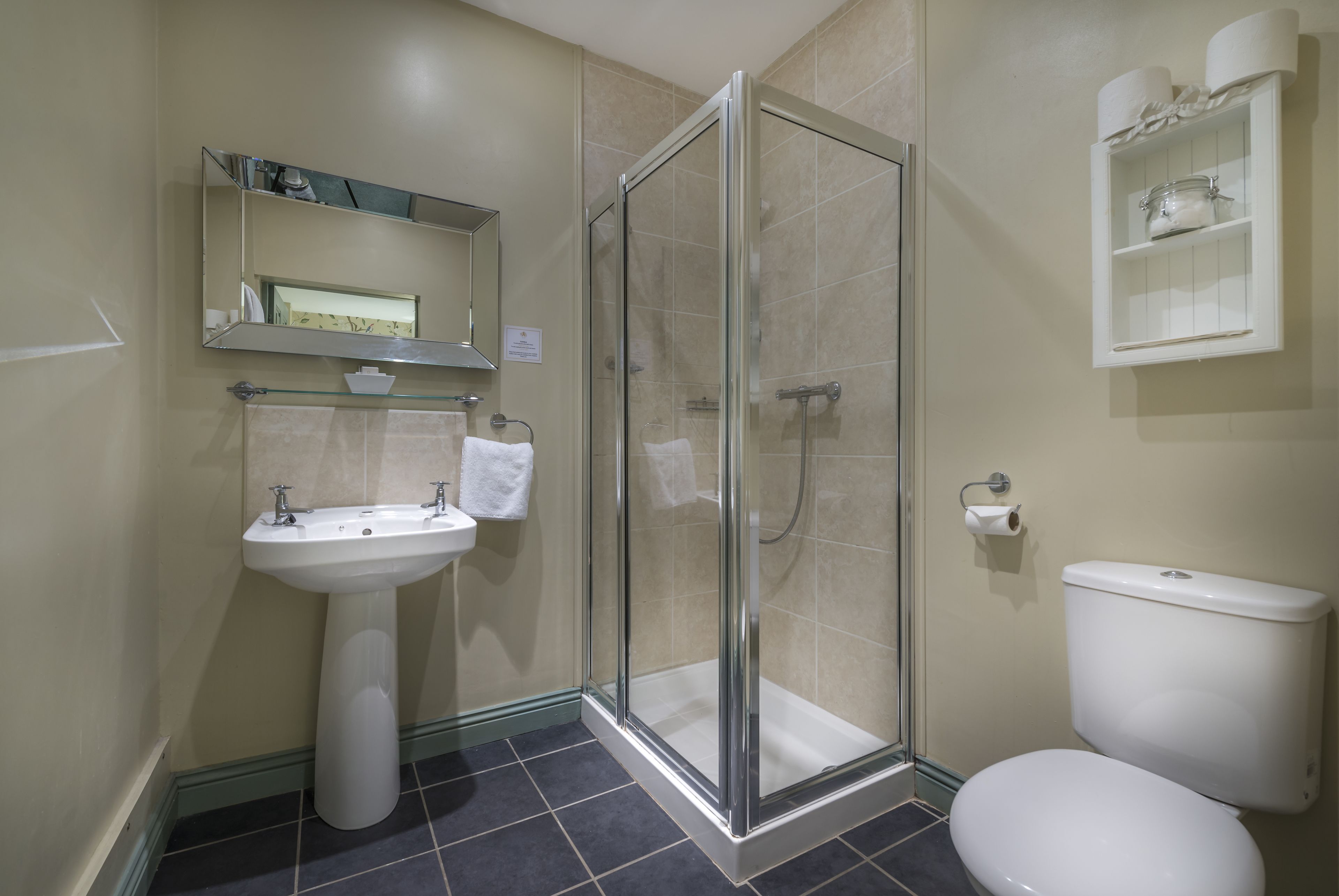 Une salle de bain avec une douche à parois de verre, un lavabo sur colonne et des toilettes.