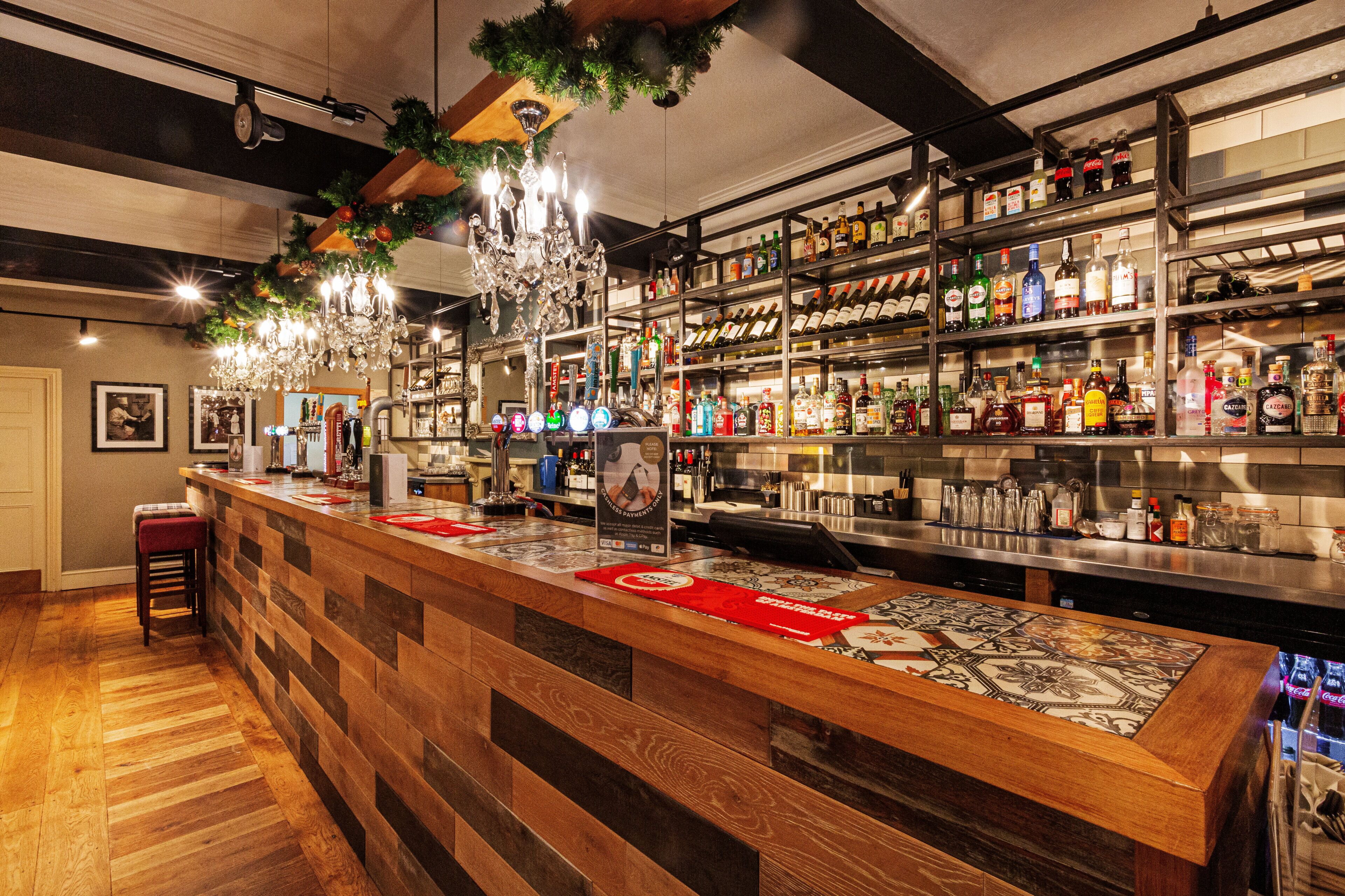 Eine Bar mit einer Holztheke, Regalen voller Spirituosenflaschen und einem Kronleuchter.