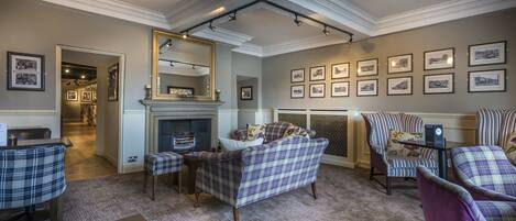 A cozy living room with a fireplace, plaid furniture, and framed pictures on the walls.