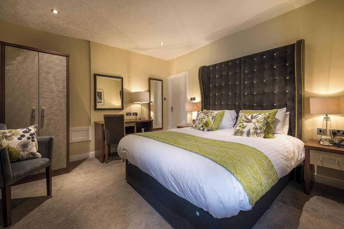 A spacious bedroom with a large bed, a wardrobe, a desk, and a chair.