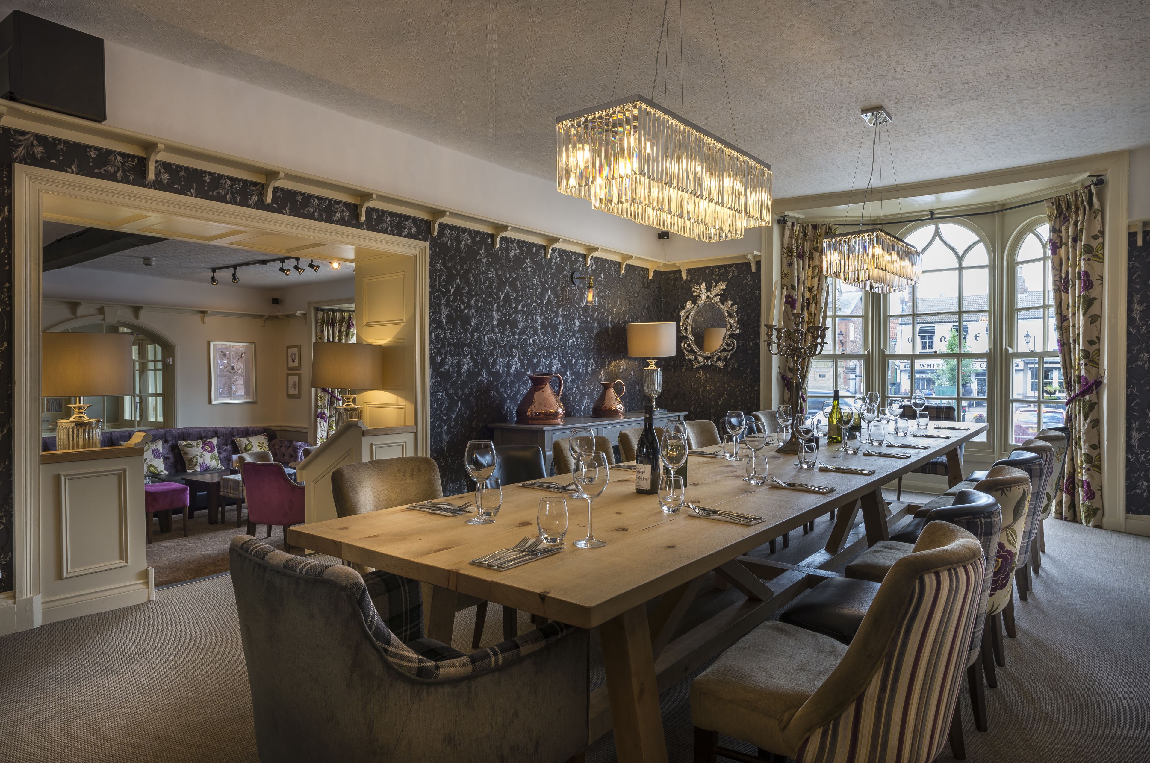 A dining area with a long wooden table set for a meal, surrounded by upholstered chairs.