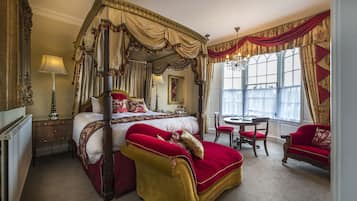 A luxurious bedroom with a four-poster bed, a sitting area with a red sofa, and a dining table.