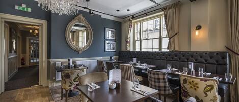 Un restaurant doté d’un lustre, d’un grand miroir et d’un coin salon confortable avec un banc et des tables.