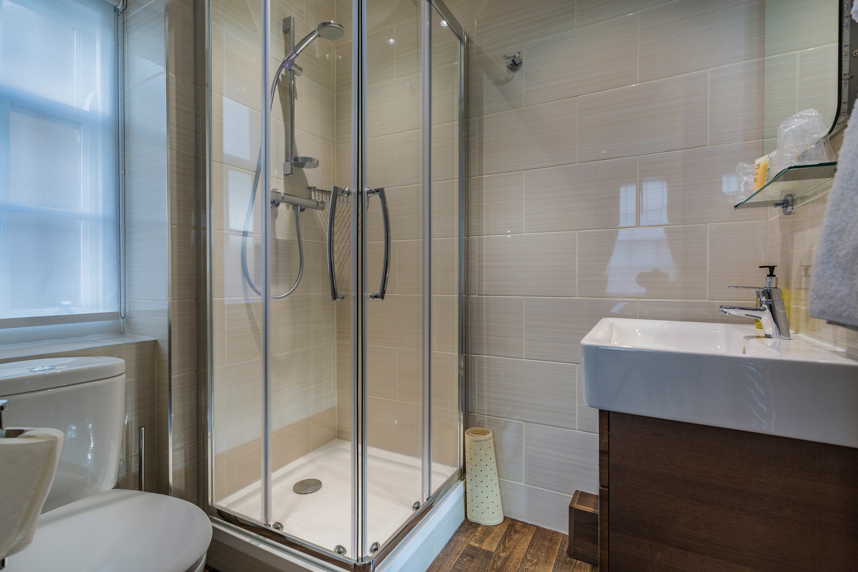 A modern bathroom with a glass-enclosed shower, a white sink, and a wooden vanity.