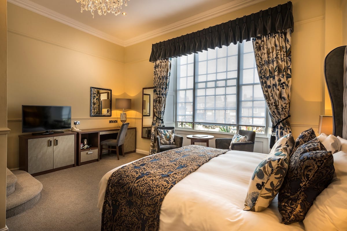 A hotel room with a large bed, a desk with a television, a chair, and a small table.