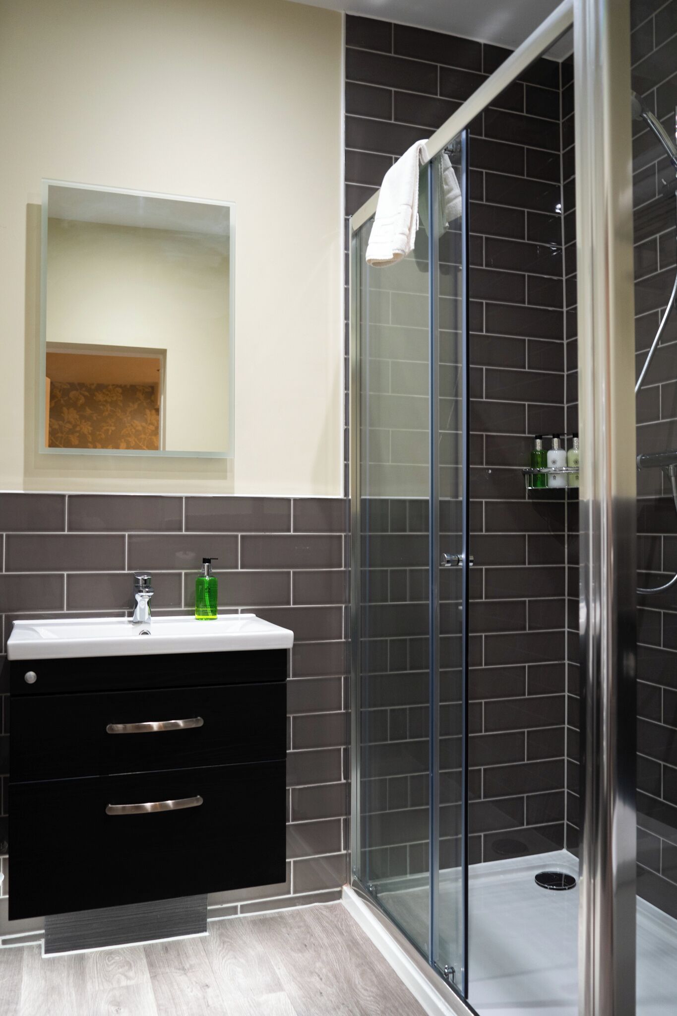 A modern bathroom with a glass shower enclosure, a black vanity with drawers, and a mirror above the sink.