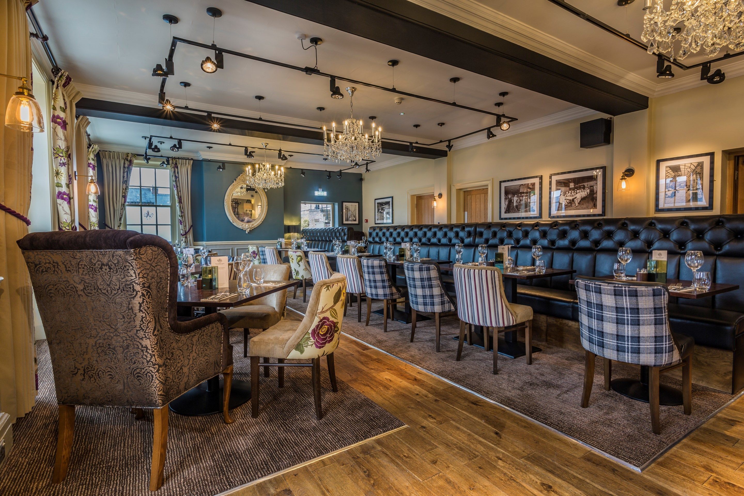 A restaurant with a blue wall, a mirror, and a chandelier. There are tables and chairs, and a bench along the wall.