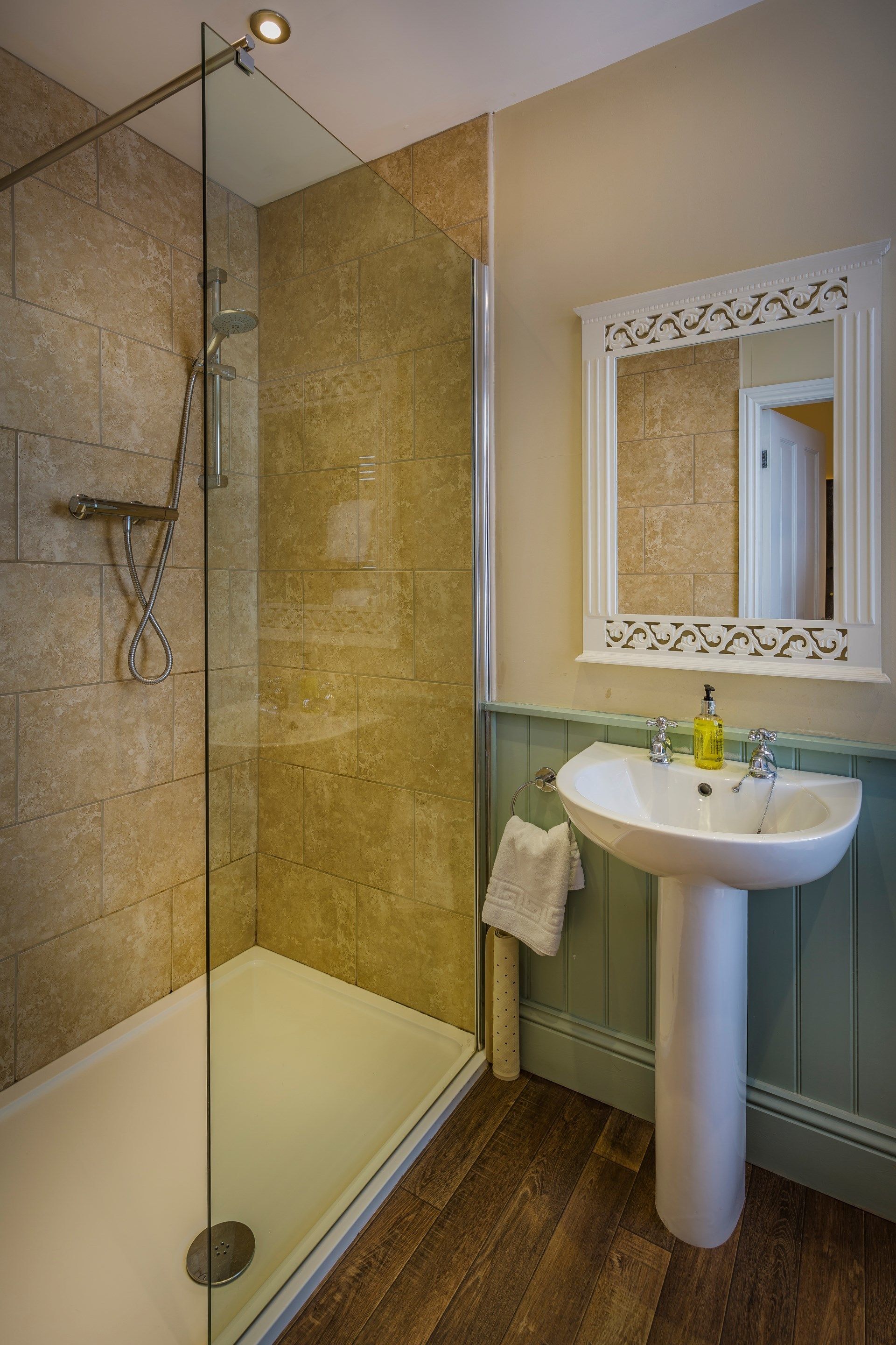 A bathroom with a glass-enclosed shower, a pedestal sink, and a mirror with a decorative frame.