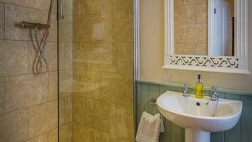 A bathroom with a glass-enclosed shower, a pedestal sink, and a mirror with a decorative frame.