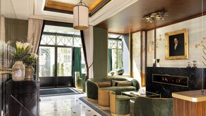 A spacious lobby with a green sofa, a wooden reception desk, and a large window offering a view of the outdoors. - Hotel Lord Byron (Paris)