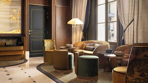 A luxurious room with a dark wooden door, a sofa set, a round table with a lamp, and a view of the city through large windows. - Hotel Lord Byron (Paris)