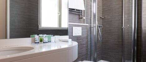 A modern bathroom with a curved white sink, a glass shower enclosure, and a toilet.