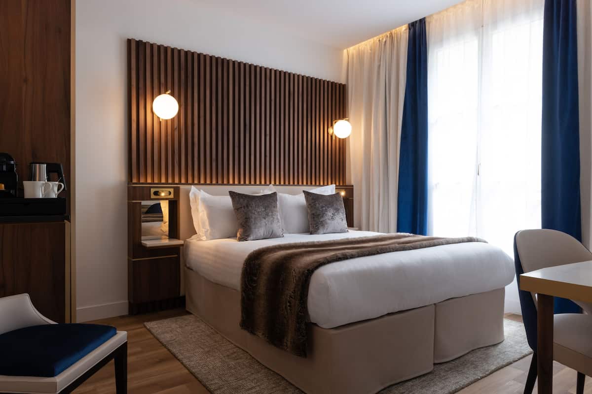 A modern hotel room with a large bed, bedside tables, a desk, and a chair.
