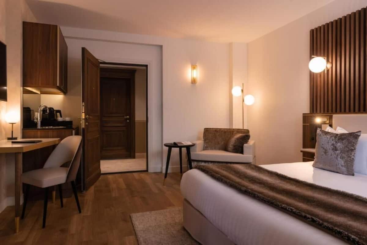 A modern hotel room with a bed, a desk, a chair, and a small table.