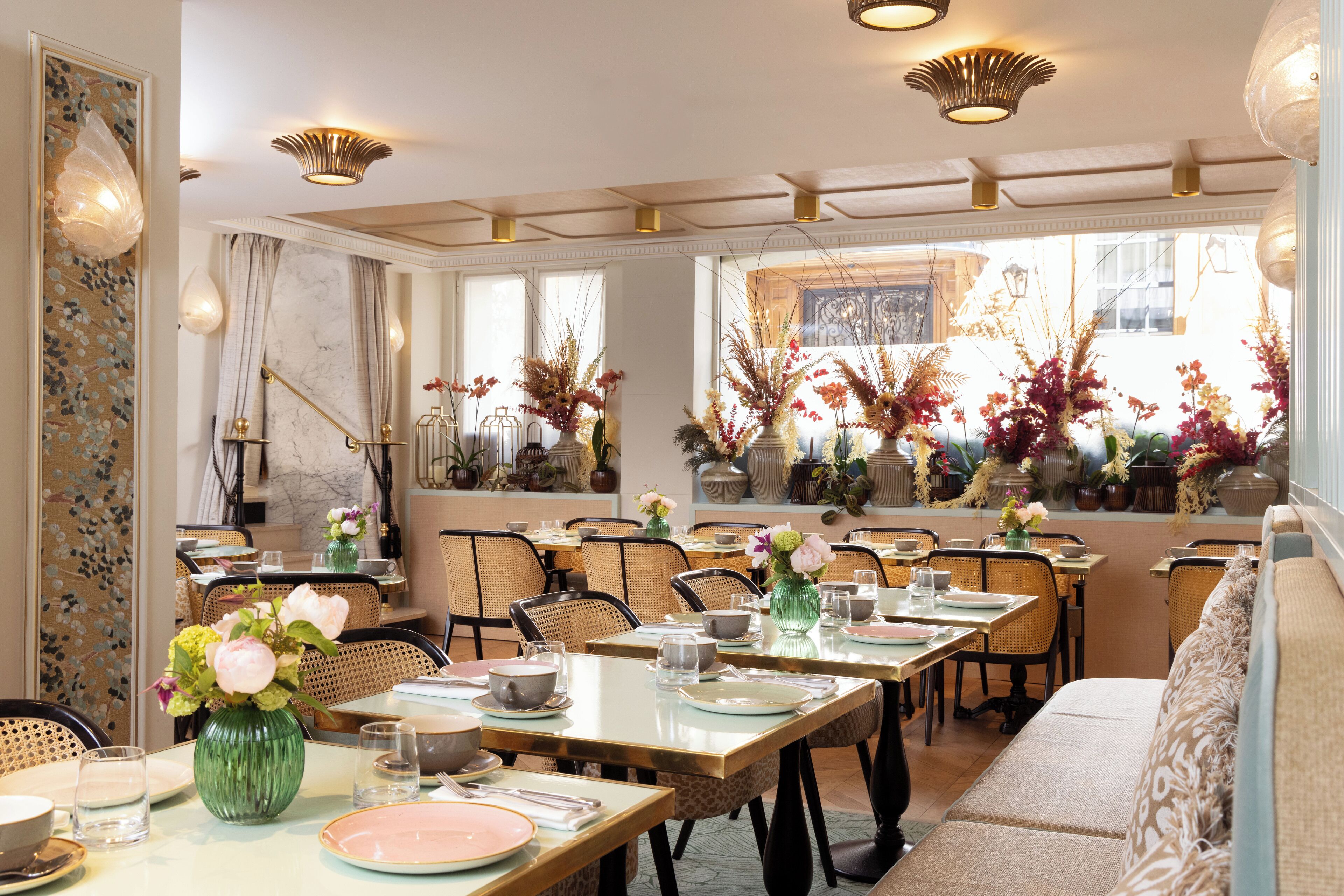 A dining area with tables set for service, chairs, and decorative plants.