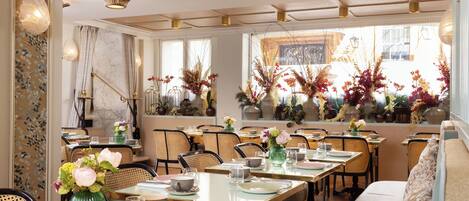 A dining area with tables set for service, chairs, and decorative plants.