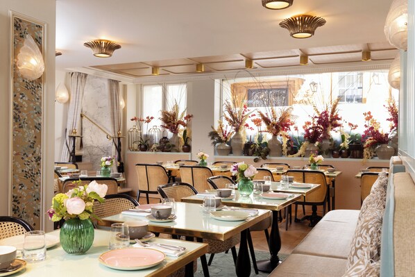 A dining area with tables set for service, chairs, and decorative plants.