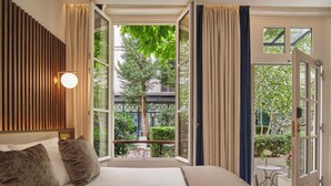 A bedroom with a large bed, a view of a balcony, and a window with curtains. - Hotel Lord Byron (Paris)