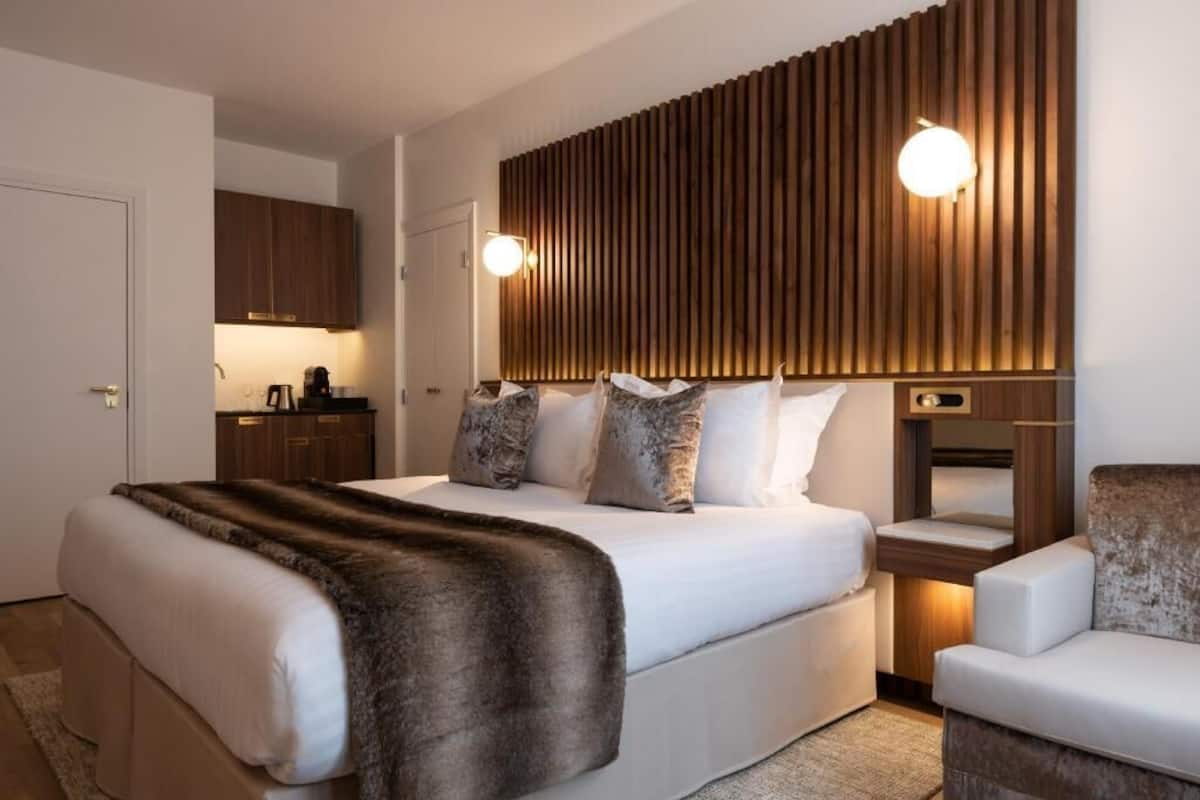 A modern hotel room with a large bed, a wooden headboard, a bedside table, and a chair.