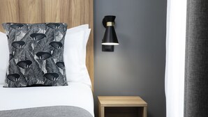 A neatly made bed with a patterned pillow, a small bedside table, and a wall-mounted lamp. - Hotel Moulin Vert (Paris)