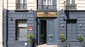 The exterior of Hotel Moulin Vert, featuring a dark blue facade, a prominent entrance with a double door, and two potted plants at the entrance. - Hotel Moulin Vert (Paris)