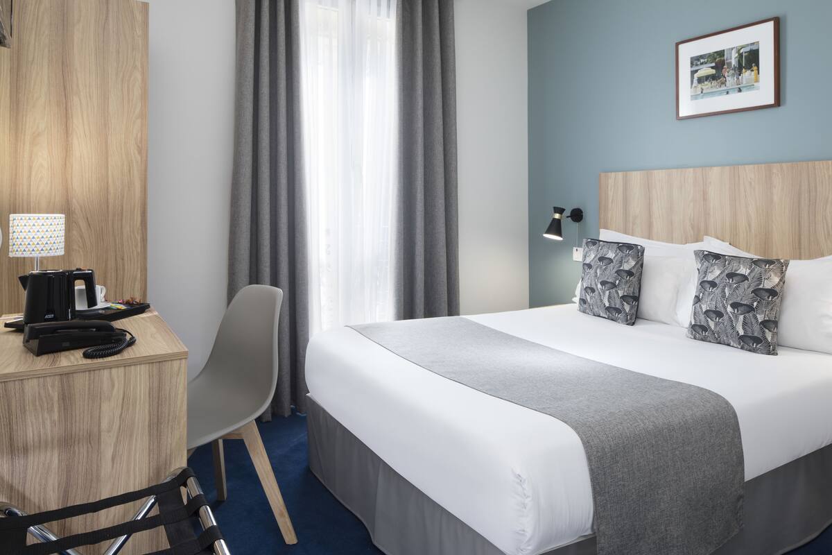 A hotel room with a bed, desk, chair, and a window with curtains.