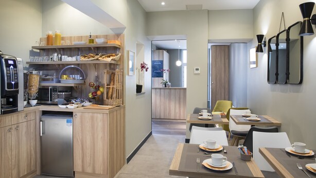 A modern kitchen with built-in appliances, wooden cabinets, and a dining area with tables set for four. - Hotel Moulin Vert (Paris)