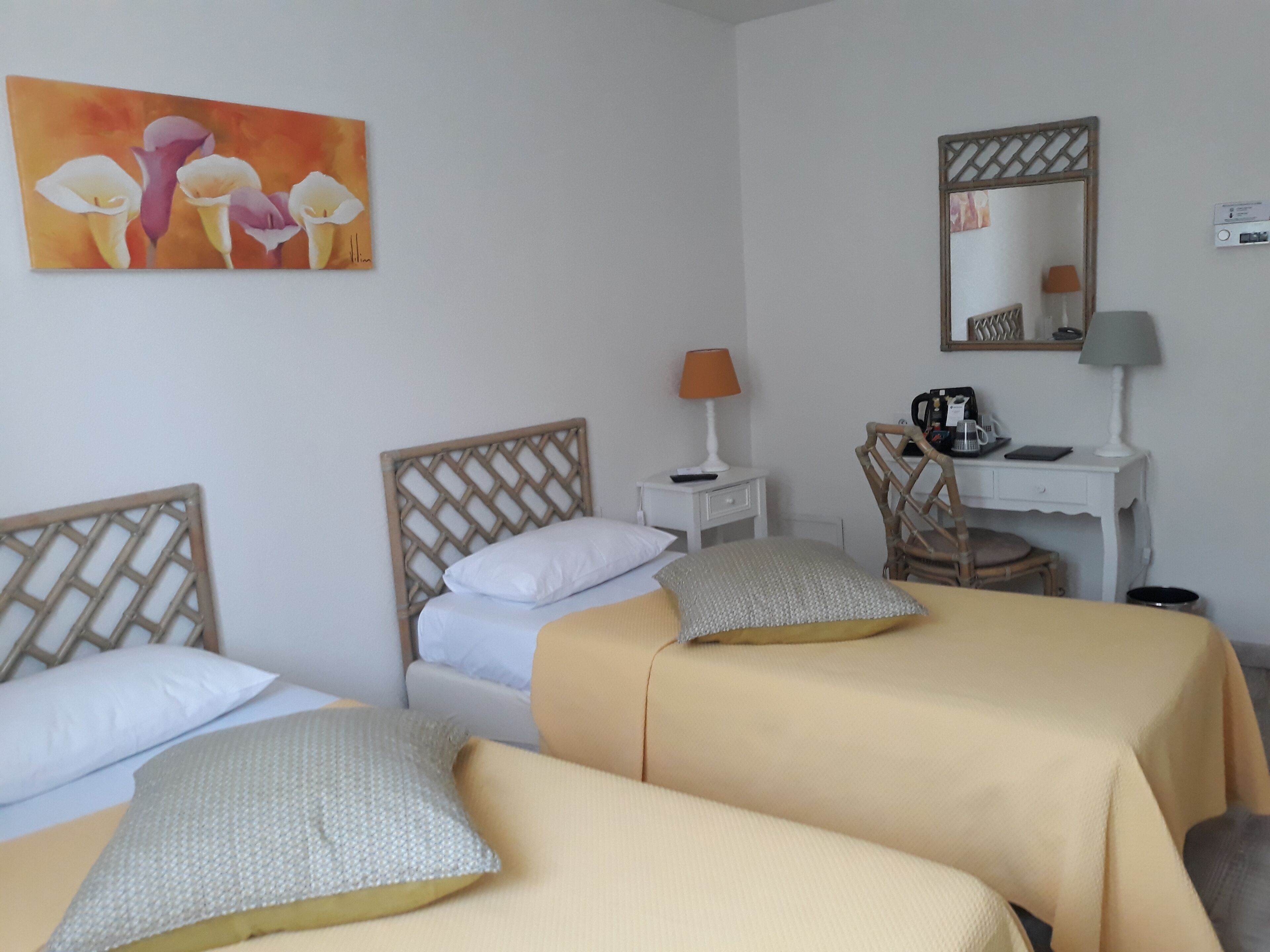 Quarto de hotel com duas camas, uma escrivaninha, uma cadeira, um abajur, um espelho e um quadro na parede.