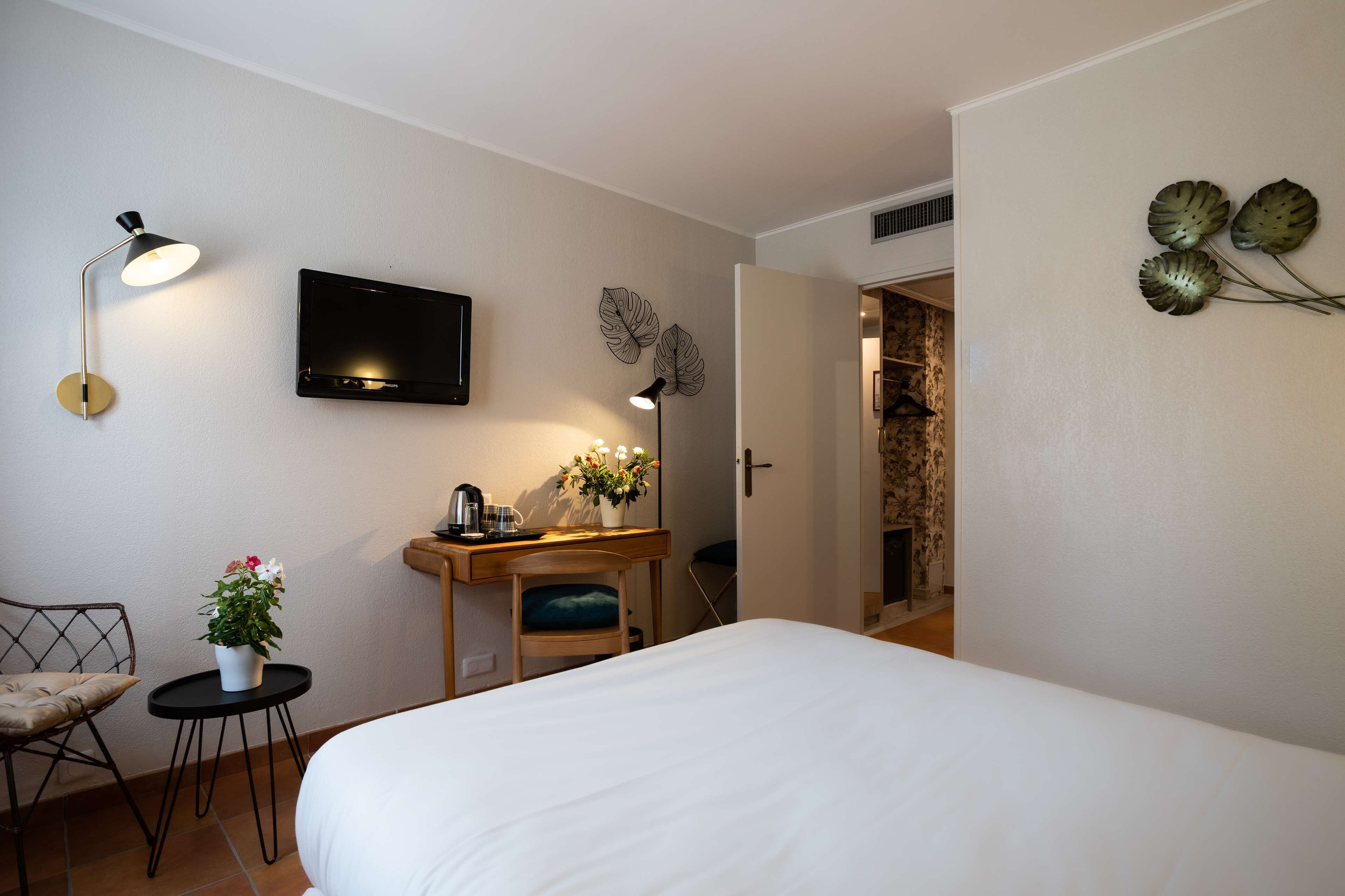 A hotel room with a bed, a desk with a chair, a TV, and a small table with a plant.