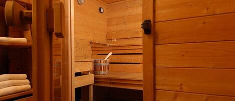 Un sauna de madera con toallas en estantes y un cubo con una cuchara.