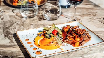 Una mesa de comedor con un plato de comida, vasos y una botella de vino.