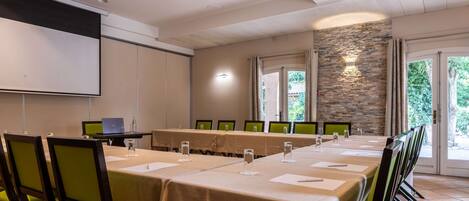 Un salón de conferencias con una larga mesa, sillas, una pantalla de proyector y una pared de piedra.