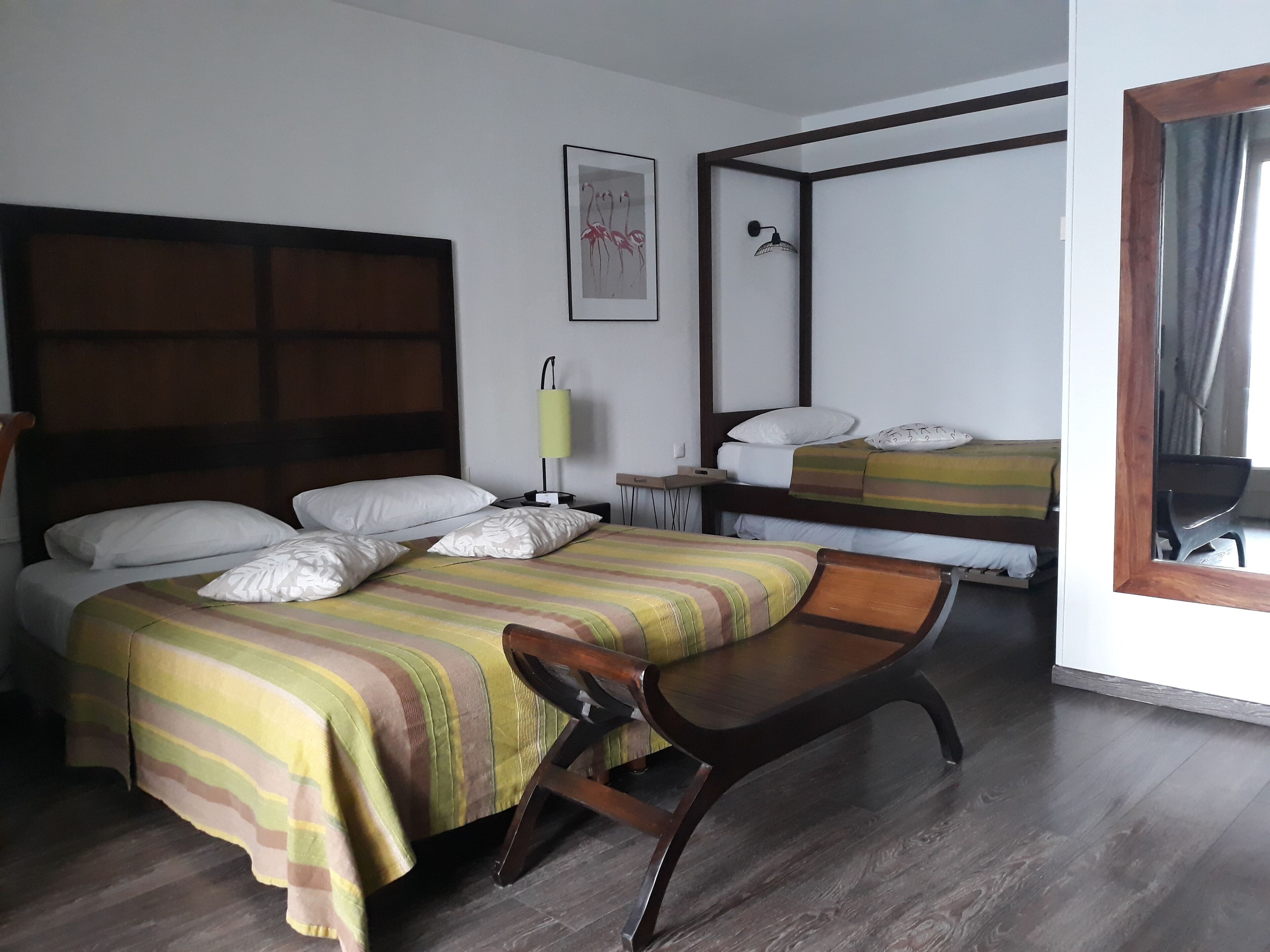 Habitación de hotel con dos camas, un escritorio, una silla, una mesita de noche, una lámpara y un espejo.