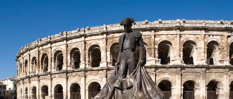 A statue in front of an ancient amphitheater with multiple arches and columns.
