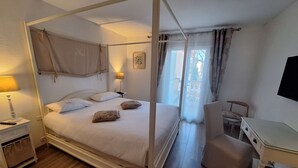 A four-poster bed with a canopy, a desk with a chair, a bedside table with a lamp, and a window with curtains. - Best Western l'Orangerie (Nîmes)