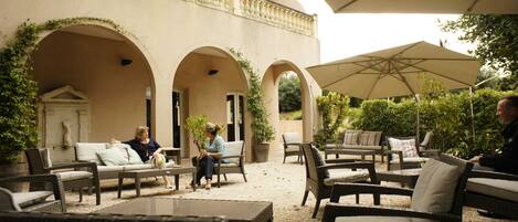 An outdoor patio area with wicker furniture, a covered seating area, and a building with arches and a balcony.