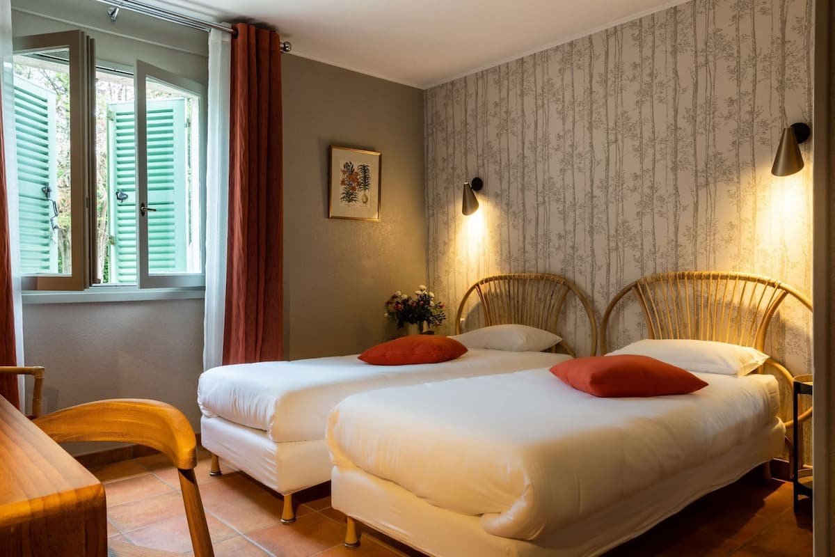 A bedroom with two beds, a wooden chair, a desk, and a window with curtains.