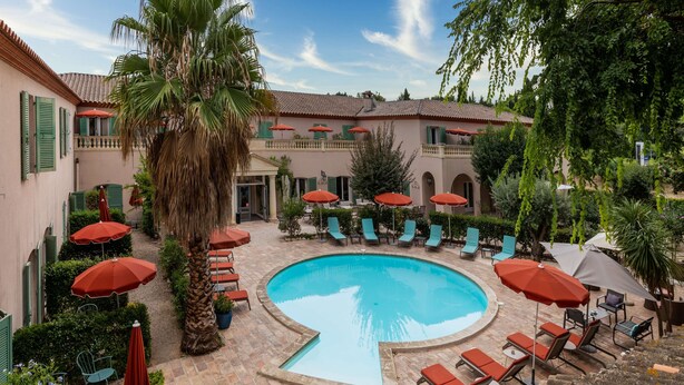 A pool area with lounge chairs and umbrellas, surrounded by a building with green shutters and a tiled roof. - Best Western l'Orangerie (Nîmes)