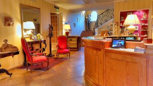 A lobby with a reception desk, a red chair, a wooden reception desk, a staircase, and a statue. - Best Western l'Orangerie (Nîmes)