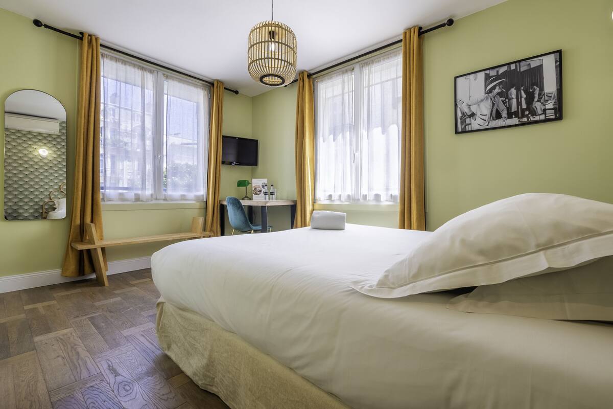 Une chambre d’hôtel avec un grand lit, un bureau, une chaise, une télévision et une fenêtre avec des rideaux.