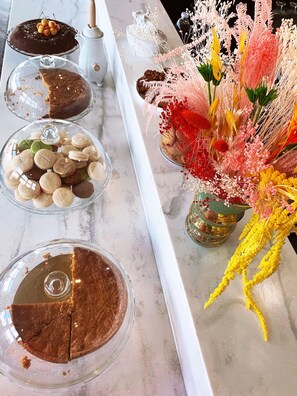 Una encimera de mármol con un pastel, macarons y un arreglo floral decorativo.