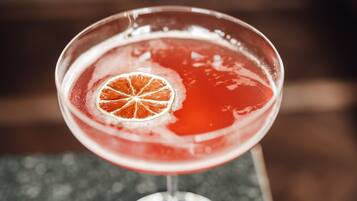 Un verre à martini contenant une boisson rouge et décoré d’une tranche d’orange, posé sur une surface en granit.