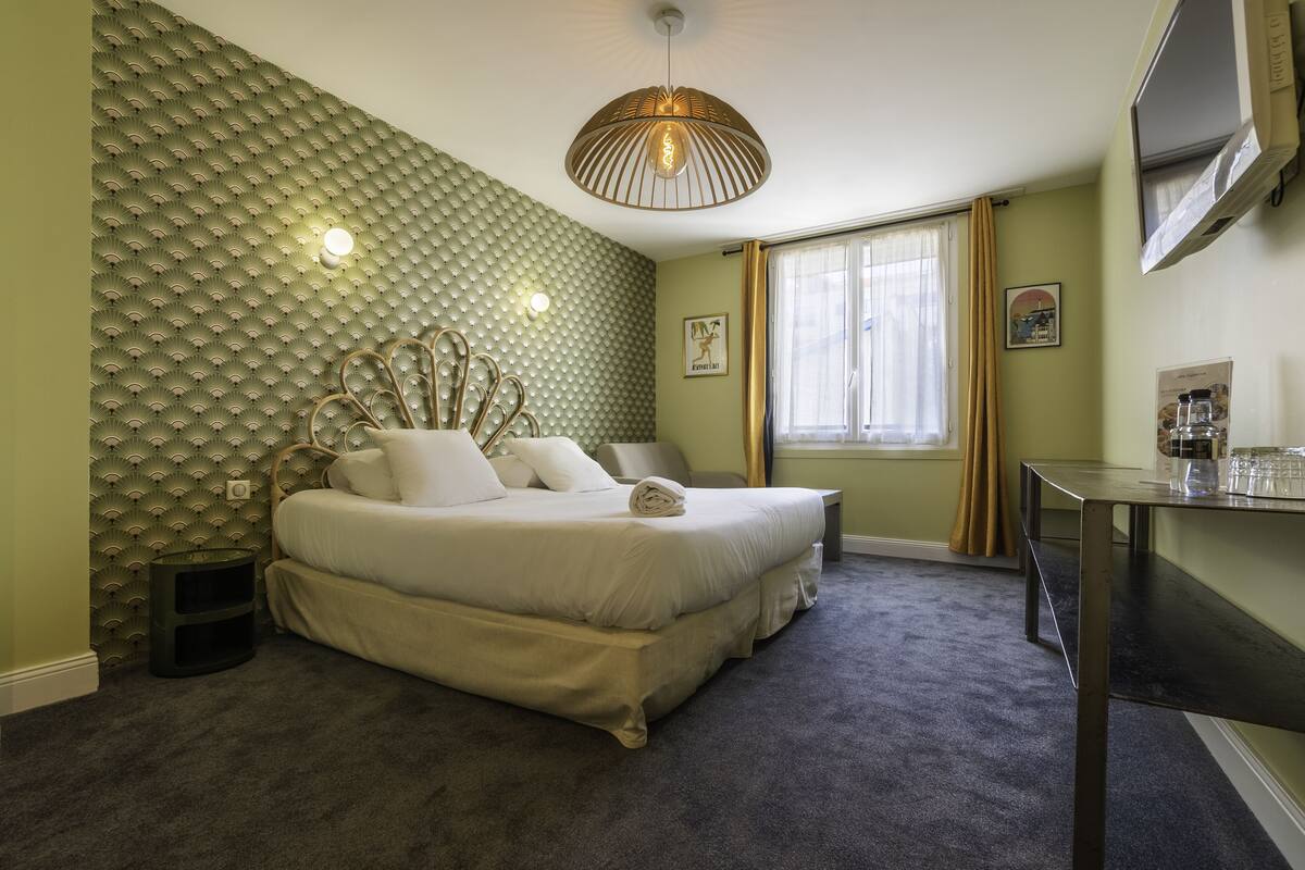 Une chambre à coucher avec un lit, une table de chevet, une lampe et une fenêtre avec des rideaux.
