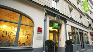 A hotel entrance with a large arched window, a small potted plant, and a sign indicating the hotel name. - ibis Styles Paris Cadet Lafayette (Paris)