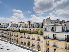 Una hilera de edificios de apartamentos parisinos con balcones, bajo un cielo parcialmente nublado.