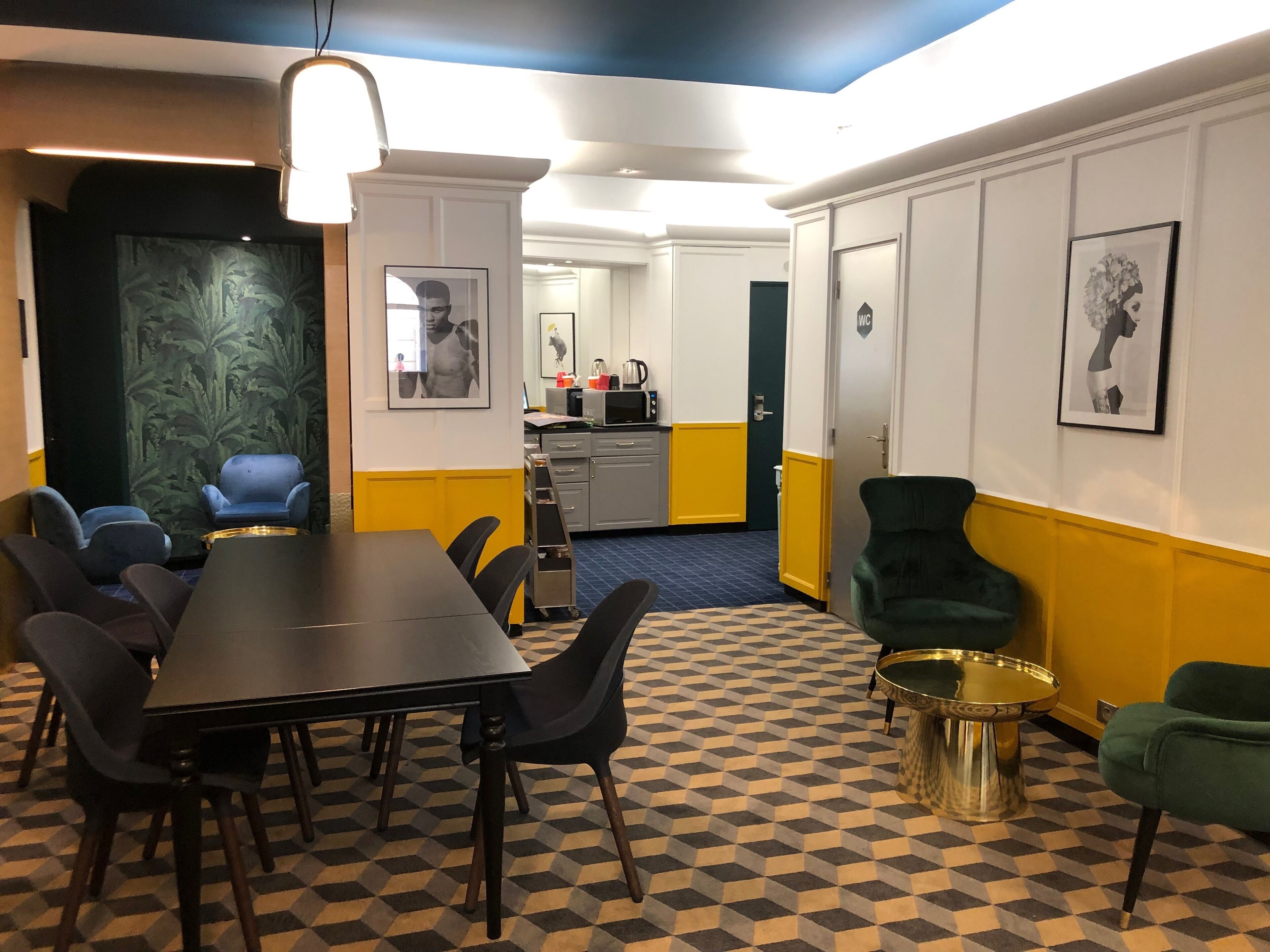 A conference room with a checkered floor, a long table with chairs, a small side table, and a green armchair.