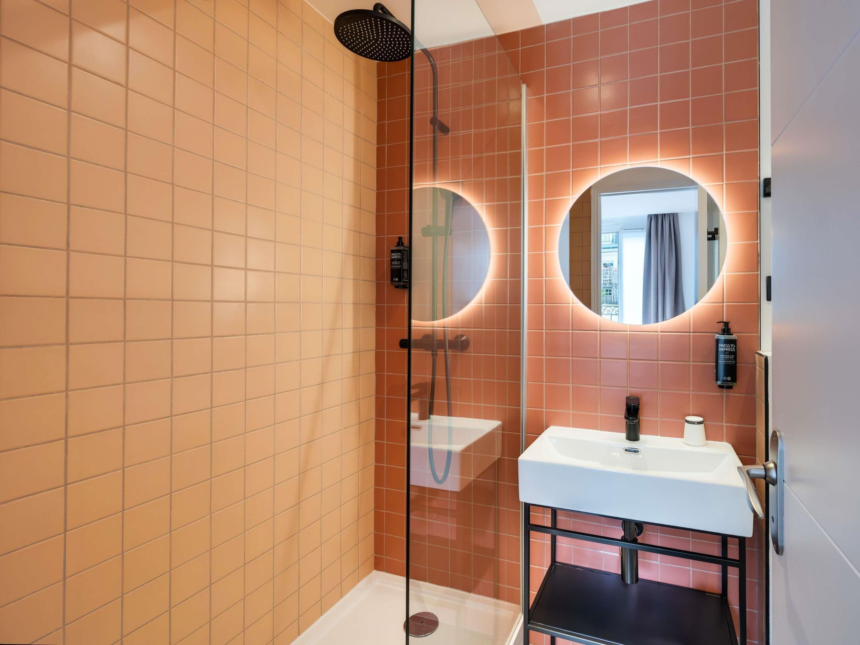 Une salle de bain moderne dotée d’une douche à parois de verre, d’un lavabo blanc et d’un miroir rond avec éclairage intégré.