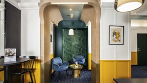 A modern interior with a checkered floor, two blue armchairs, a small round table, and a hanging light fixture. - ibis Styles Paris Cadet Lafayette (Paris)