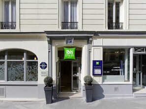 Een hotelingang met een groen bord, een kleine potplant en een raam met uitzicht.